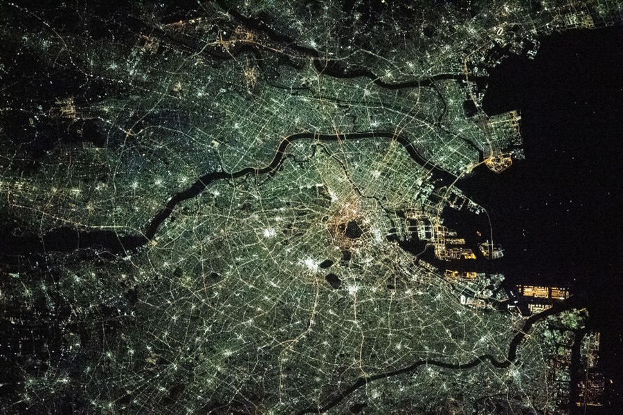 The streets, rivers, and city lights of Tokyo are visible from above, at night.