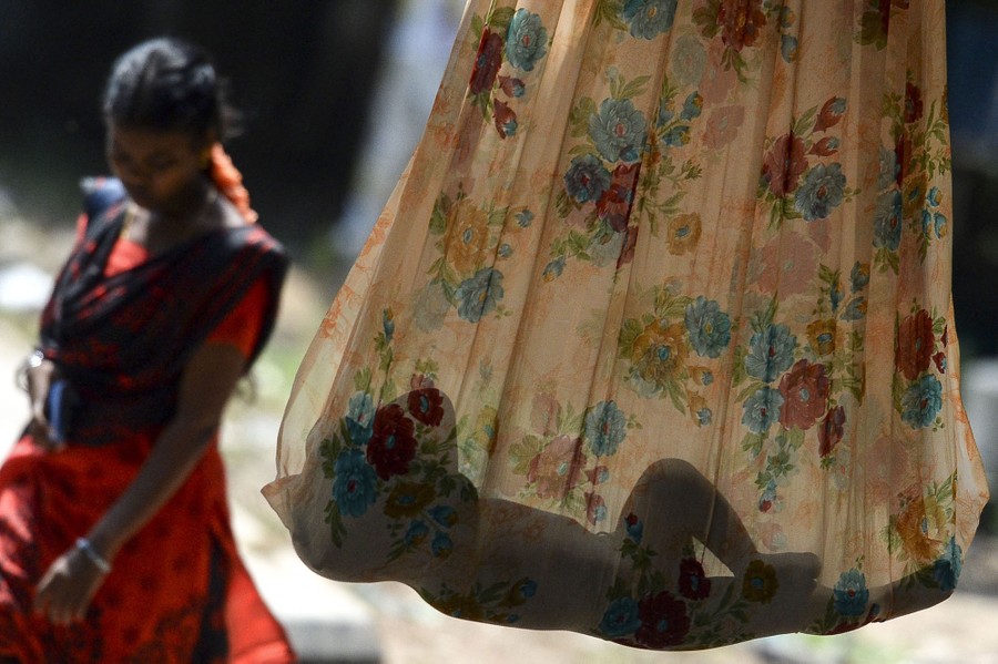 A woman walks past as a small child sleeps in a makeshift hammock made from a single sheet of fabric.