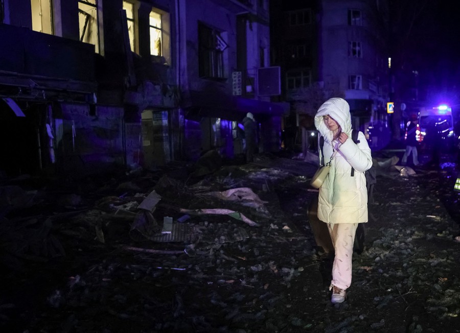 A person walks away from debris and damaged buildings in a city street.