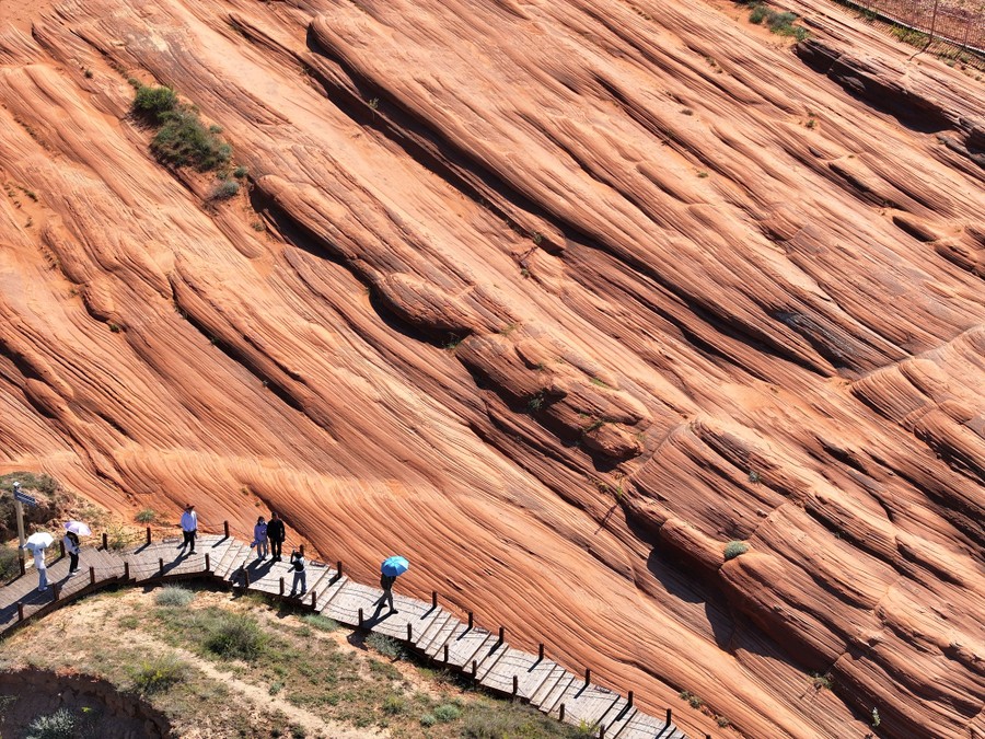 An elevated view of tourists on a walkway overlooking a wavy, layered rock formation.