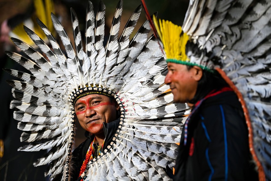 Two people are seen wearing large feather headdresses .