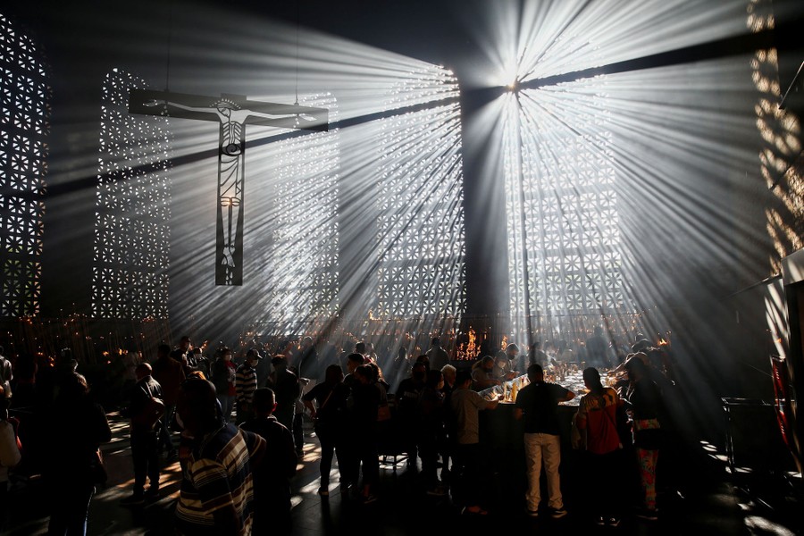 People light candles inside a church amid rays of light flooding into the slightly smoky room.