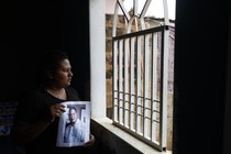 Photo of a woman staring out of a window while holding a photo of a man