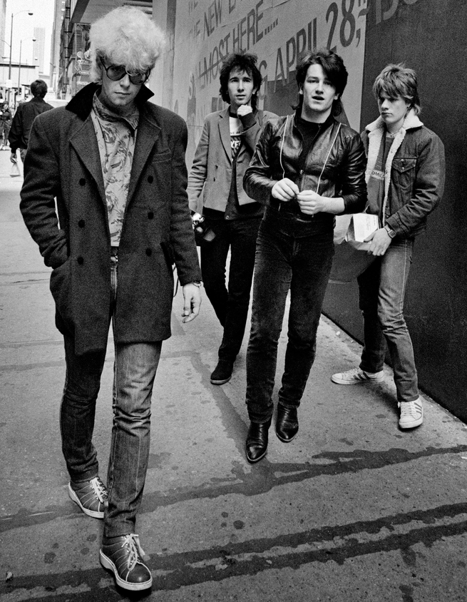 black-and-white photo of band members in coats on urban sidewalk