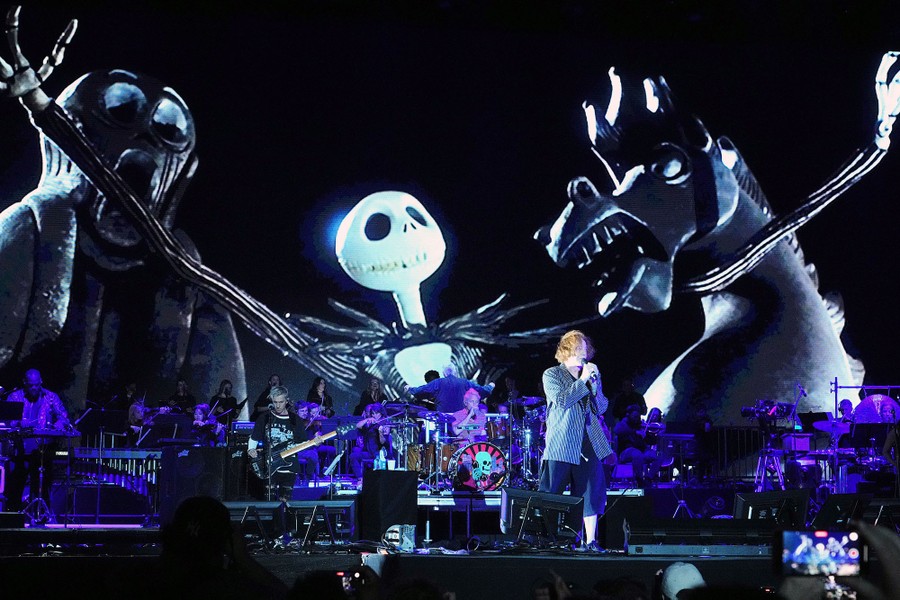 A scene from the movie "The Nightmare Before Christmas" is displayed on a screen behind Danny Elfman and a band onstage.