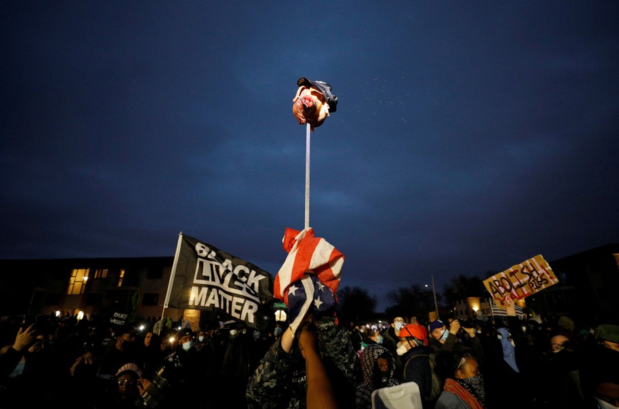 Protesters hold up a pig's head on a stick, wearing a police cap.