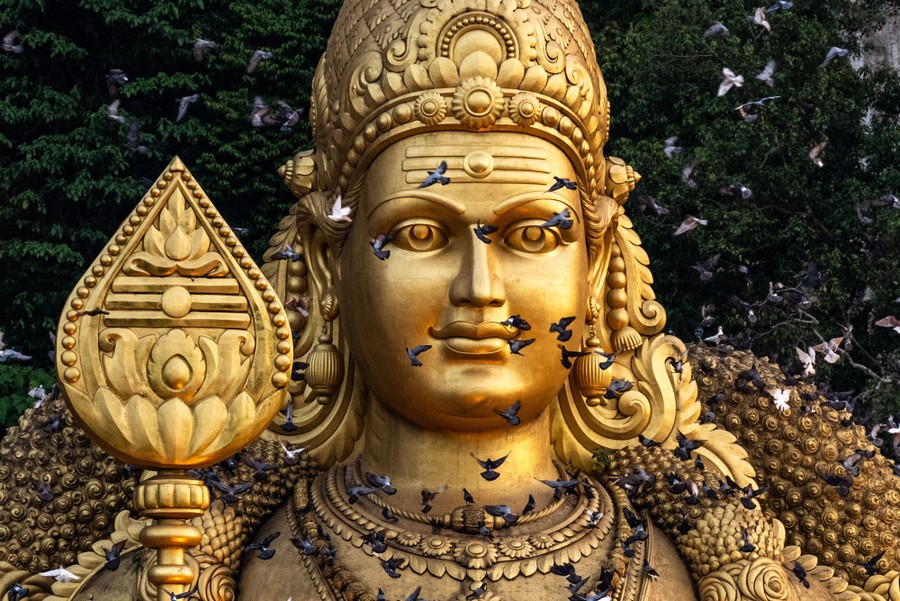 Pigeons fly in front of a large golden statue.