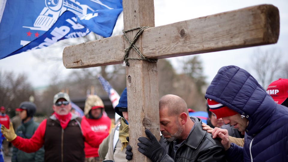 Supporters of President Donald Trump pray outside the U.S. Capitol on January 6, leaning on a large wooden cross.