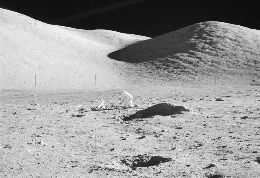 An astronaut kneels on a flat space on the moon, working on a scientific experiment.