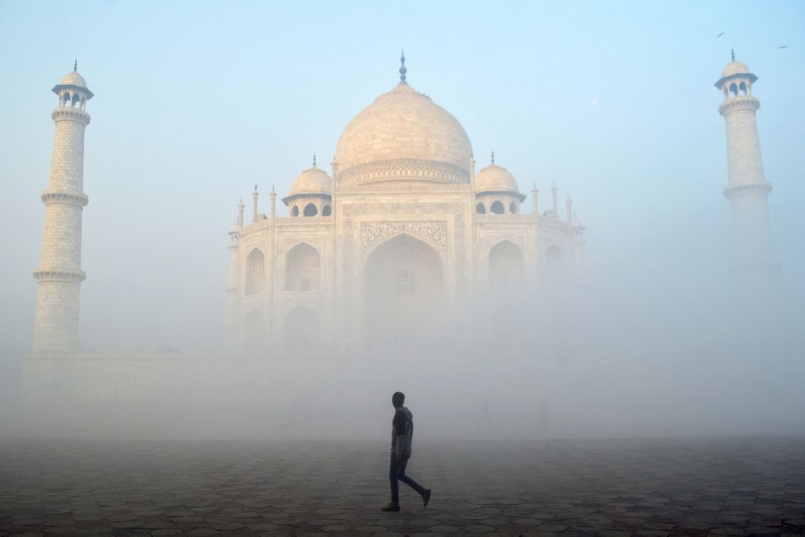 A man walks past a Taj Mahal half-enveloped in fog.