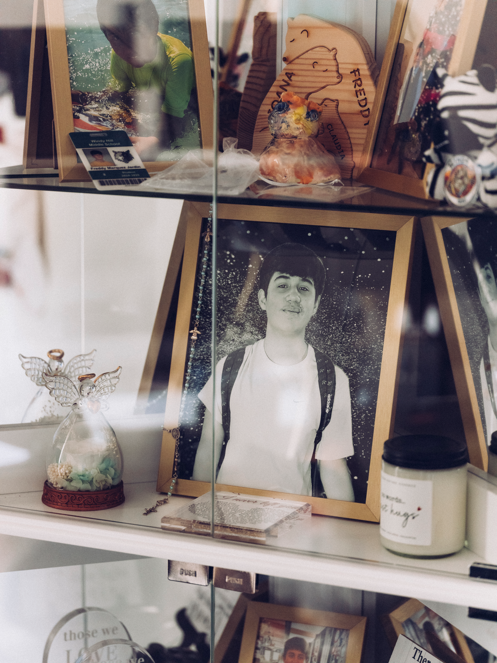 photo of glass cabinet shelves with black-and-white framed photo of young teen and other curios
