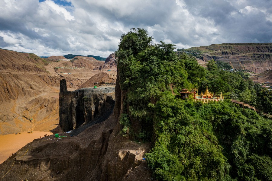 A temple stands among trees on a hill that has mostly been dug away or eroded behind it, part of a large jade mine.