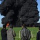 Four people watch as black smoke billows from an oil-storage site.