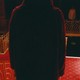 Filling the middle of the frame is the back of a person standing on a staircase, facing another person across the hall. The carpet is red, and shadows are deep.