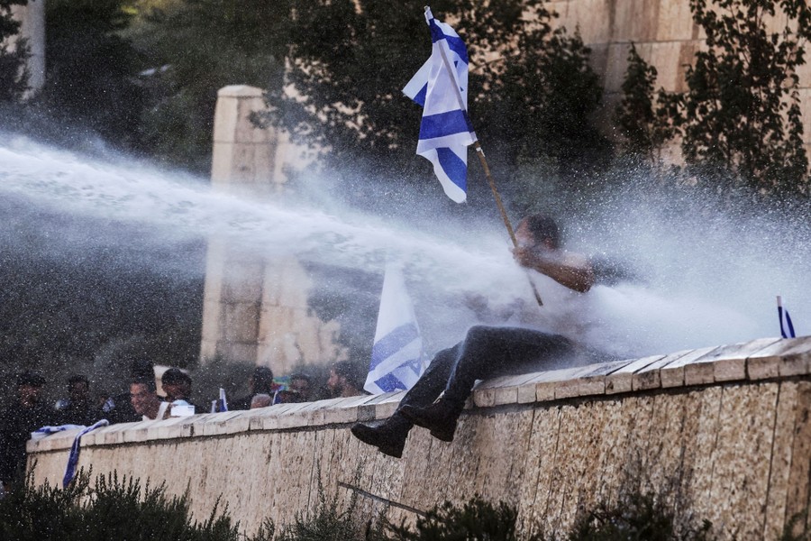A protester sitting on a stone wall is blasted with a water cannon.