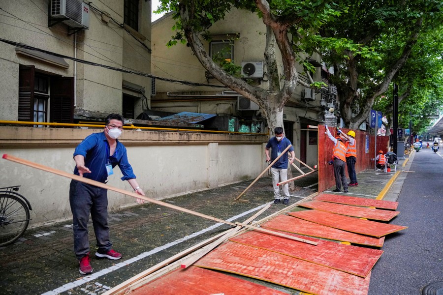 Several workers deconstruct a temporary wall on a city sidewalk.