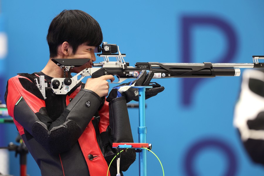 A competitor holds a complicated air rifle up to his shoulder and face.