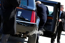 President Donald Trump climbs into a car held open by a secret service agent as exhaust comes out of the tailpipe.