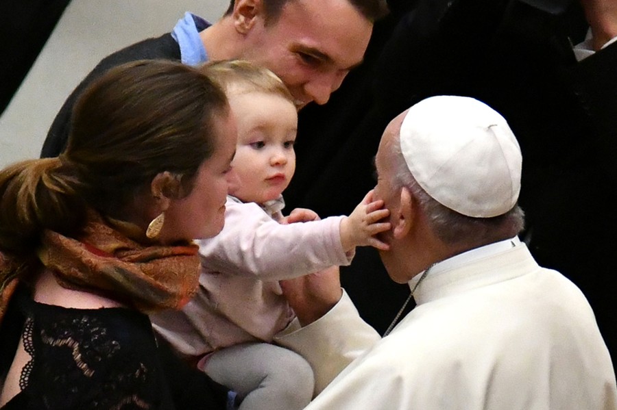 A small child, held by an adult, touches Pope Francis's face.