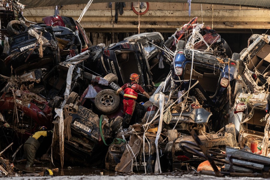 A rescue worker climbs on part of a huge pile of damaged cars and flood debris.