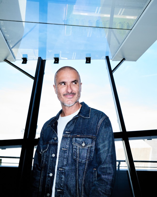 A color photograph of Zane Lowe in front of a wall of windows