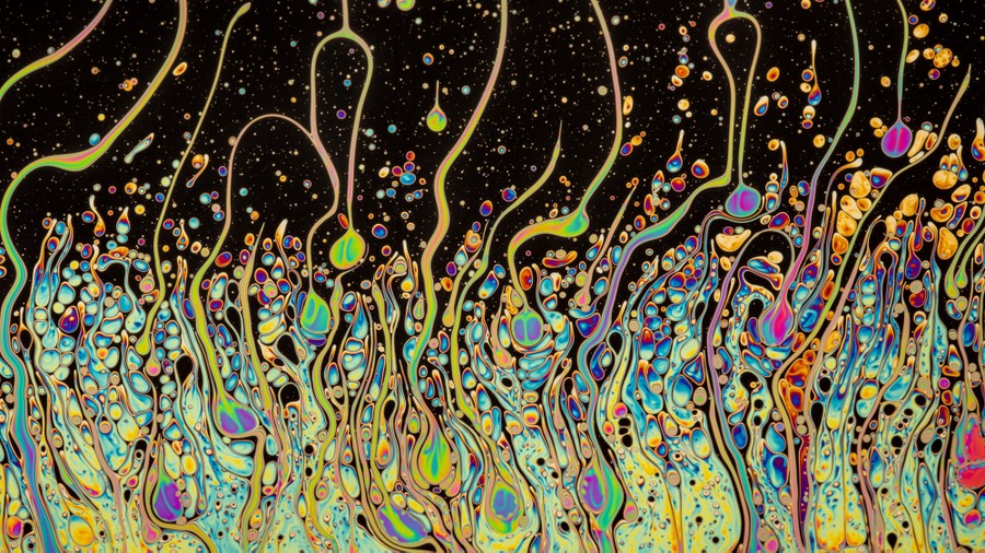 Colorful swirls and blobs form as soap interacts with water.
