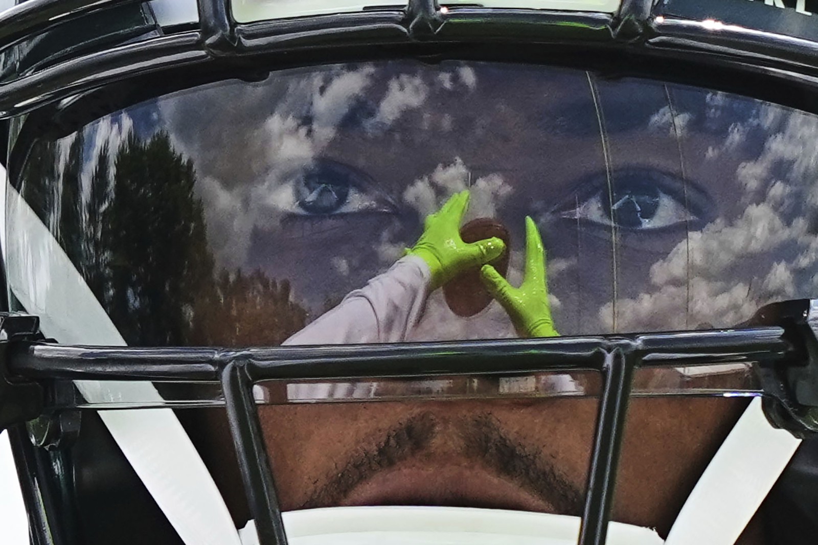 A close view of a person playing football, with their hands reflected in the visor on their helmet.
