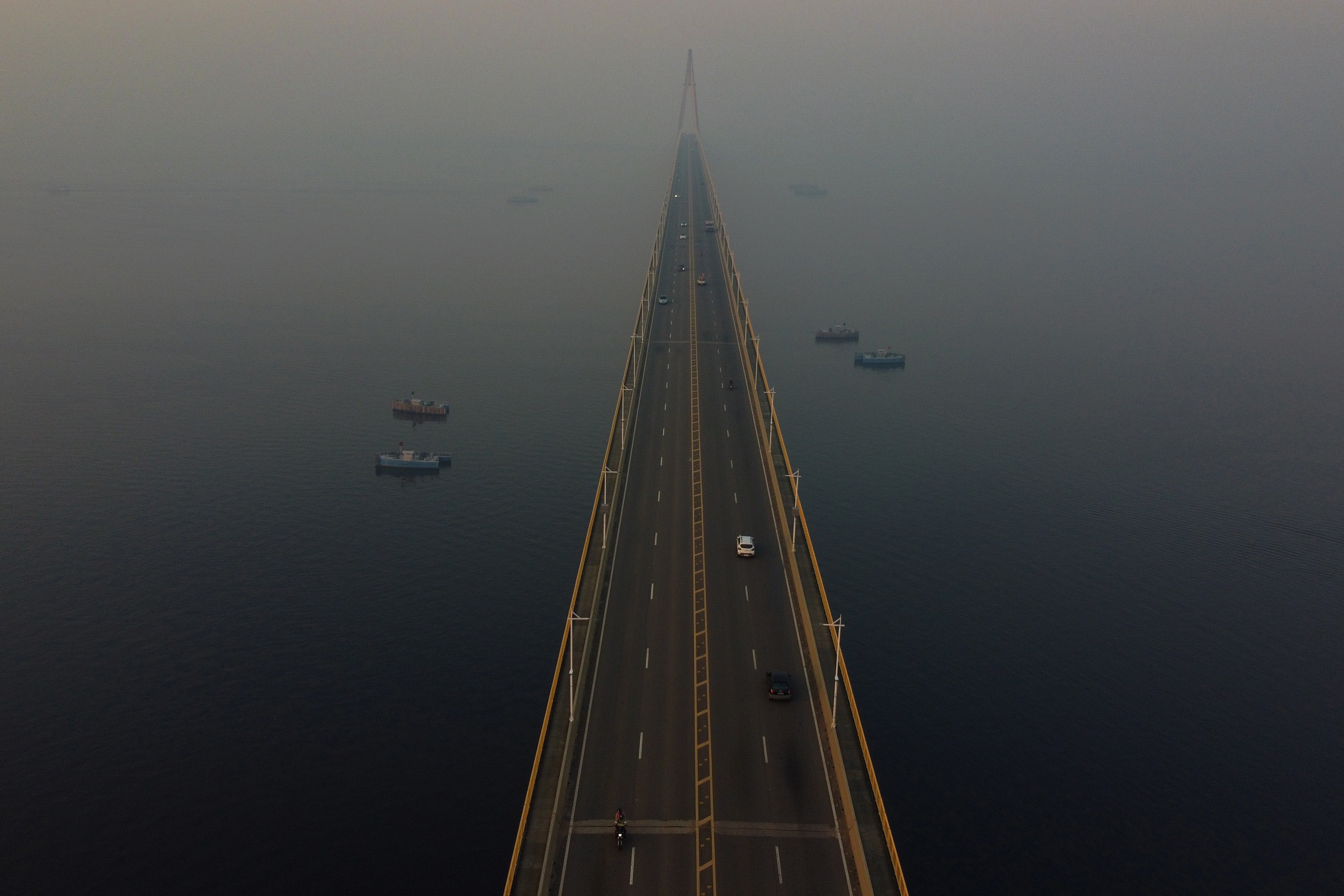 An elevated view of a long road bridge shrouded in hazy smoke.