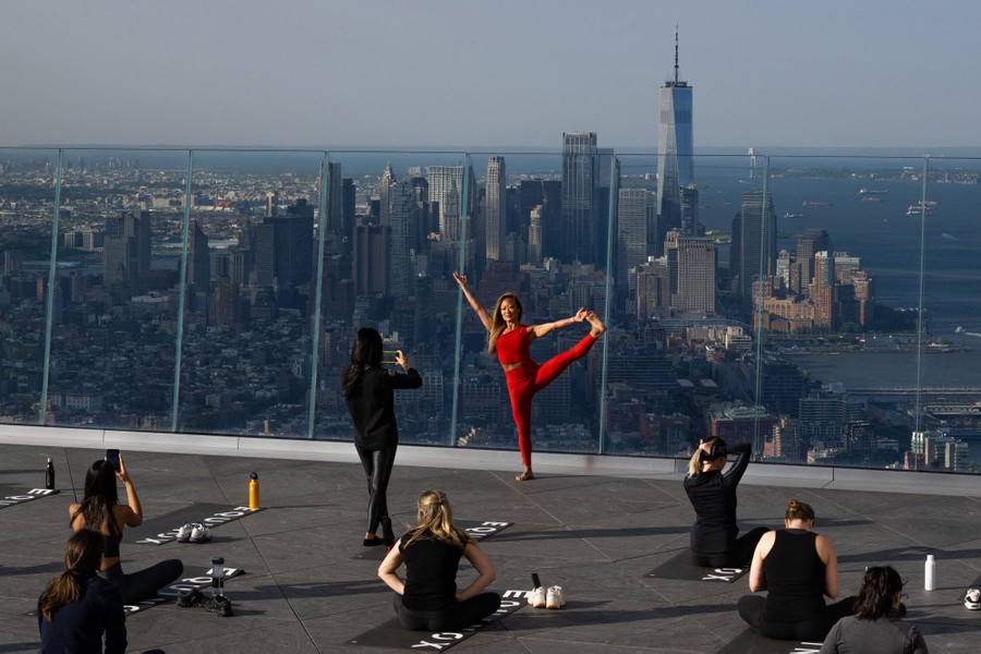 People take part in a yoga class on a high observation deck, with New York's buildings visible below.