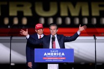 Donald Trump stands behind Mehmet Oz as Oz speaks at a podium