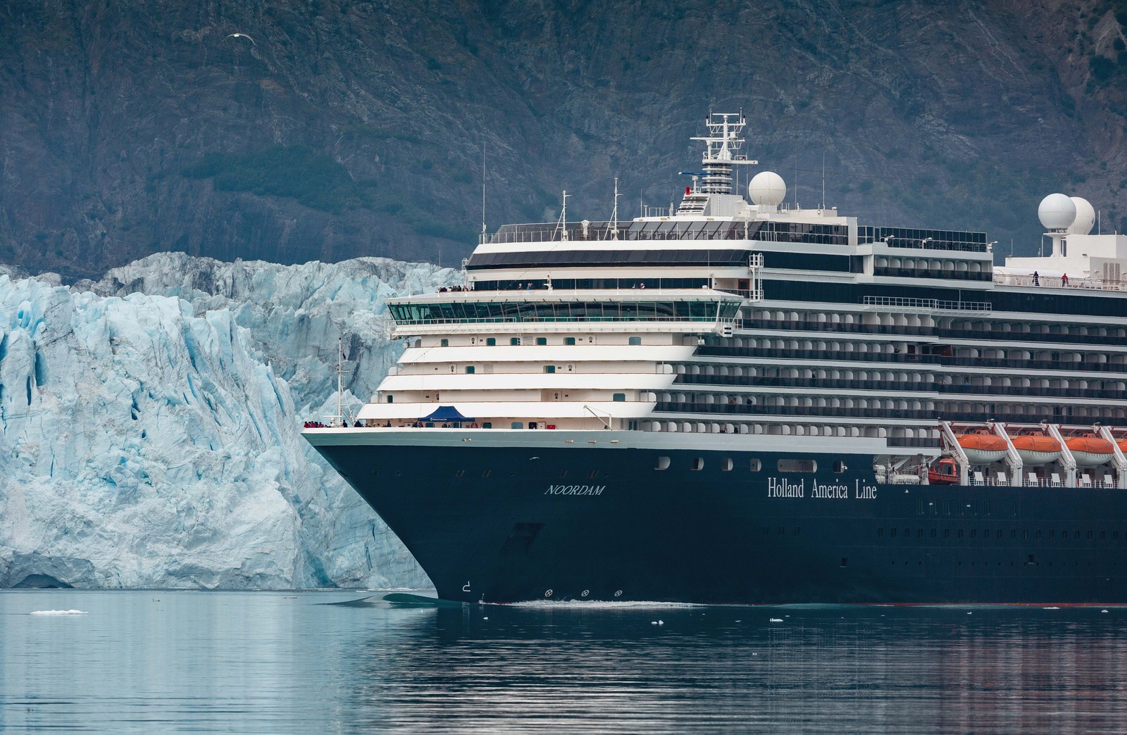 A cruise ship passes in front of the face of a tall glacier.