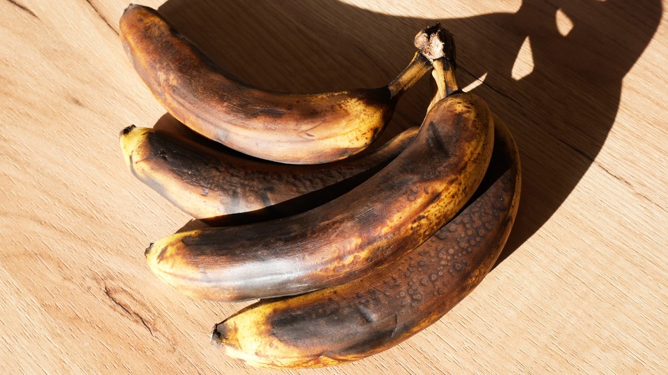 Four very brown bananas laid on their side on a wood surface