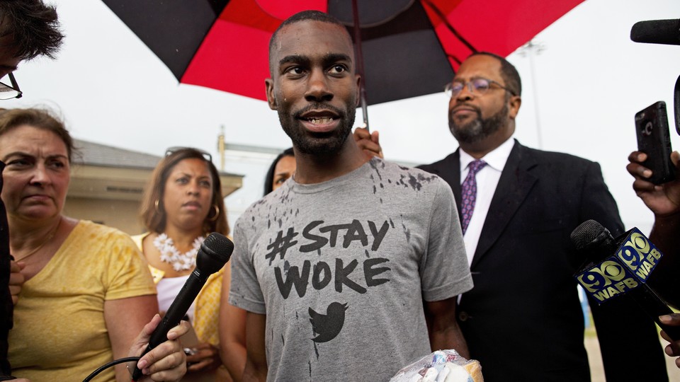 DeRay Mckesson speaks to the media, wearing a grey shirt that says 'Stay Woke.'