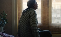 A person sits on top of a bed and gazes toward a window.