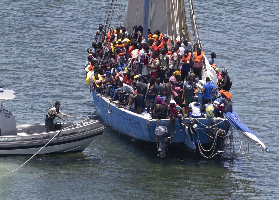 Dozens of people stand on a severely overcrowded sailboat.