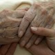 An elderly person holds hands with a younger person