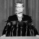 A white man in a suit stands on a podium, with his image so chopped up as to be uncrecognizable