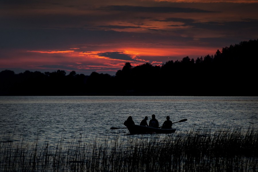Four people row in a small boat on a lake at sunset.