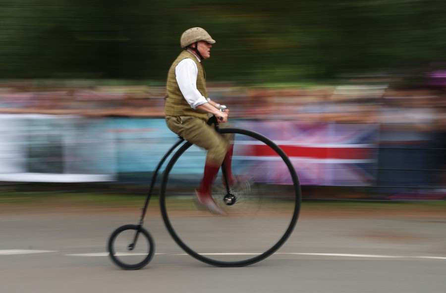 A person rides past atop an old-fashioned bicycle with a very large front wheel.