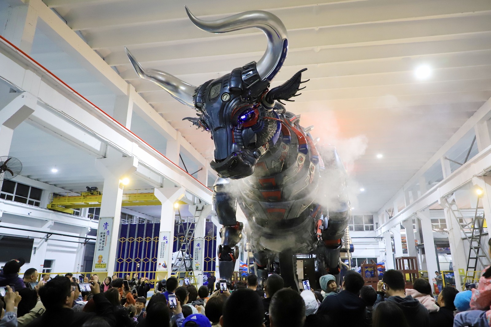 A crowd of people looks up at a large, mechanical puppet shaped like a mythical bull.