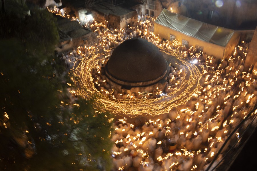 A long-exposure image of people walking in circles around a courtyard while carrying candles