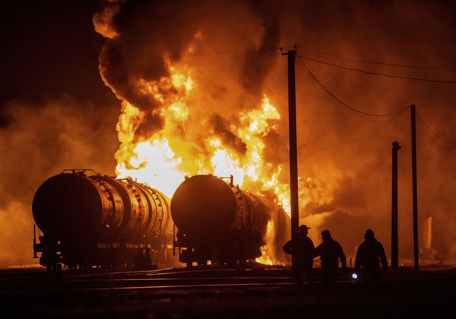 Several people watch railroad tanker cars burn at night.