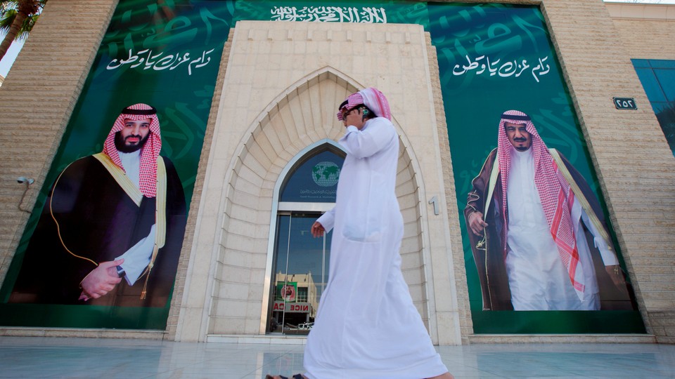 A man speaks on the phone as he walks past posters depicting Saudi Arabia's King Salman bin Abdulaziz Al Saud and Crown Prince Mohammed bin Salman.