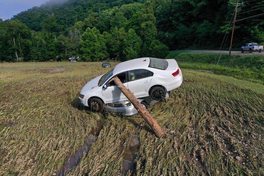 Two cars sit stacked on top of each other in a field, left there by recent flash flooding.