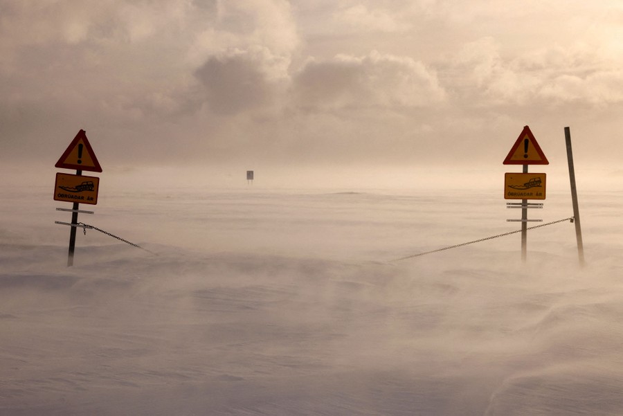 Two traffic signs stand along a closed snow-covered road.