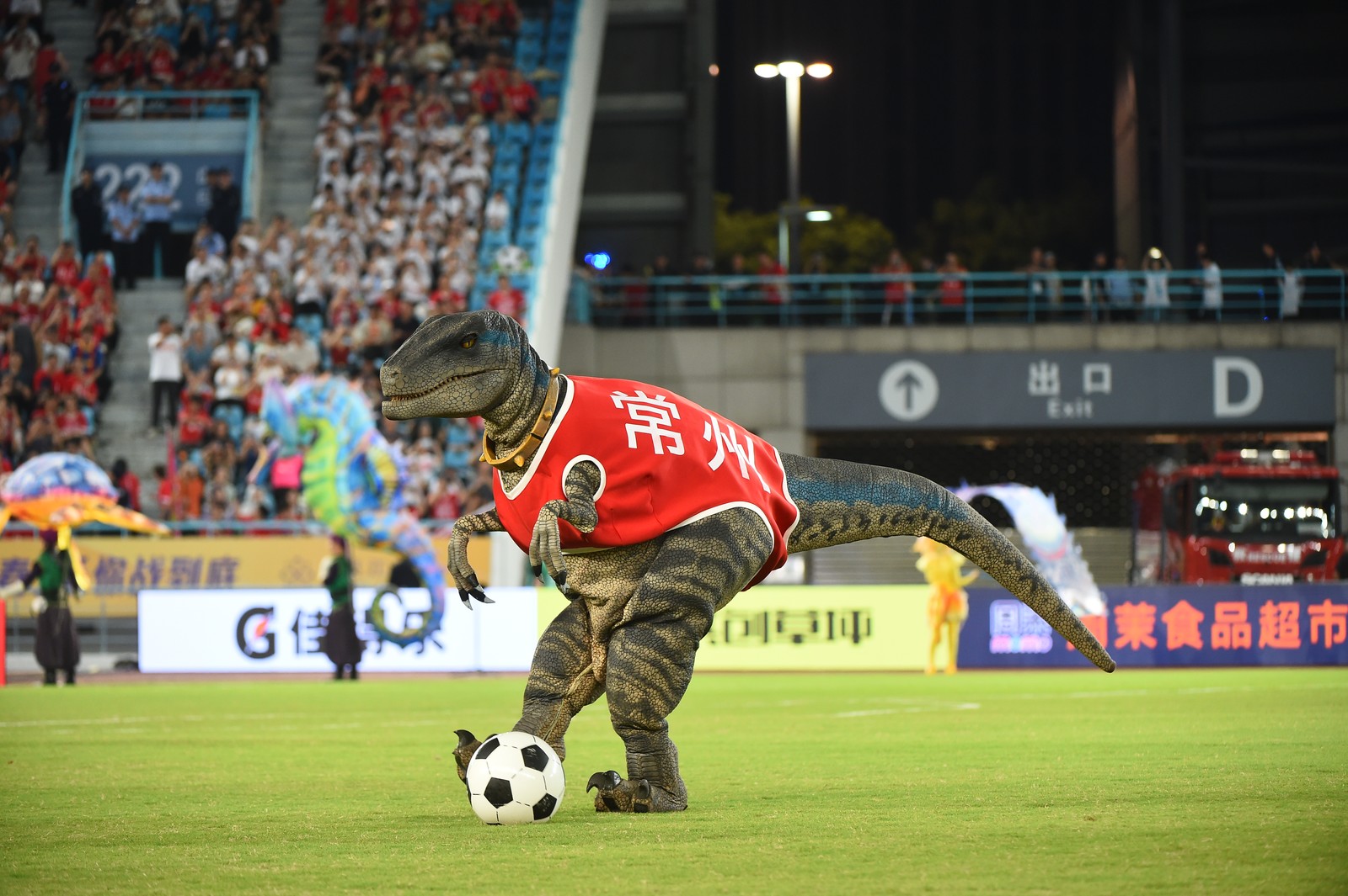A person in a T-Rex costume plays with a ball on a soccer field.