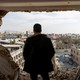 Photograph of a man looking through the side of a bombed out building.