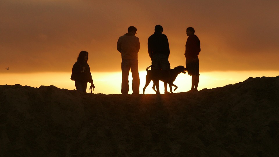 Four people and a dog are silhouetted against a sunset or sunrise.