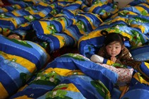 A child looks up at the camera while other children nap around her. 