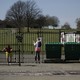 A woman removes her phone and stares through the closed gates of Brockwell Park.